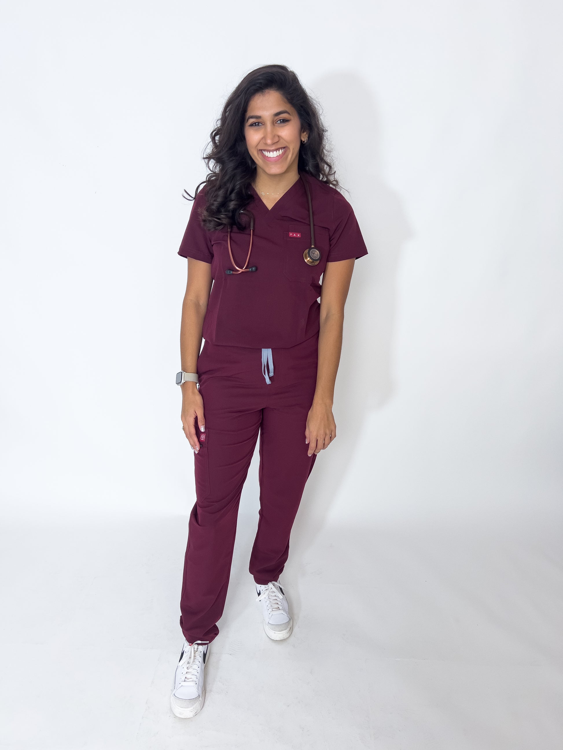 Radiant female doctor in PAX Primus crimson scrubs with stethoscope and white shoes.