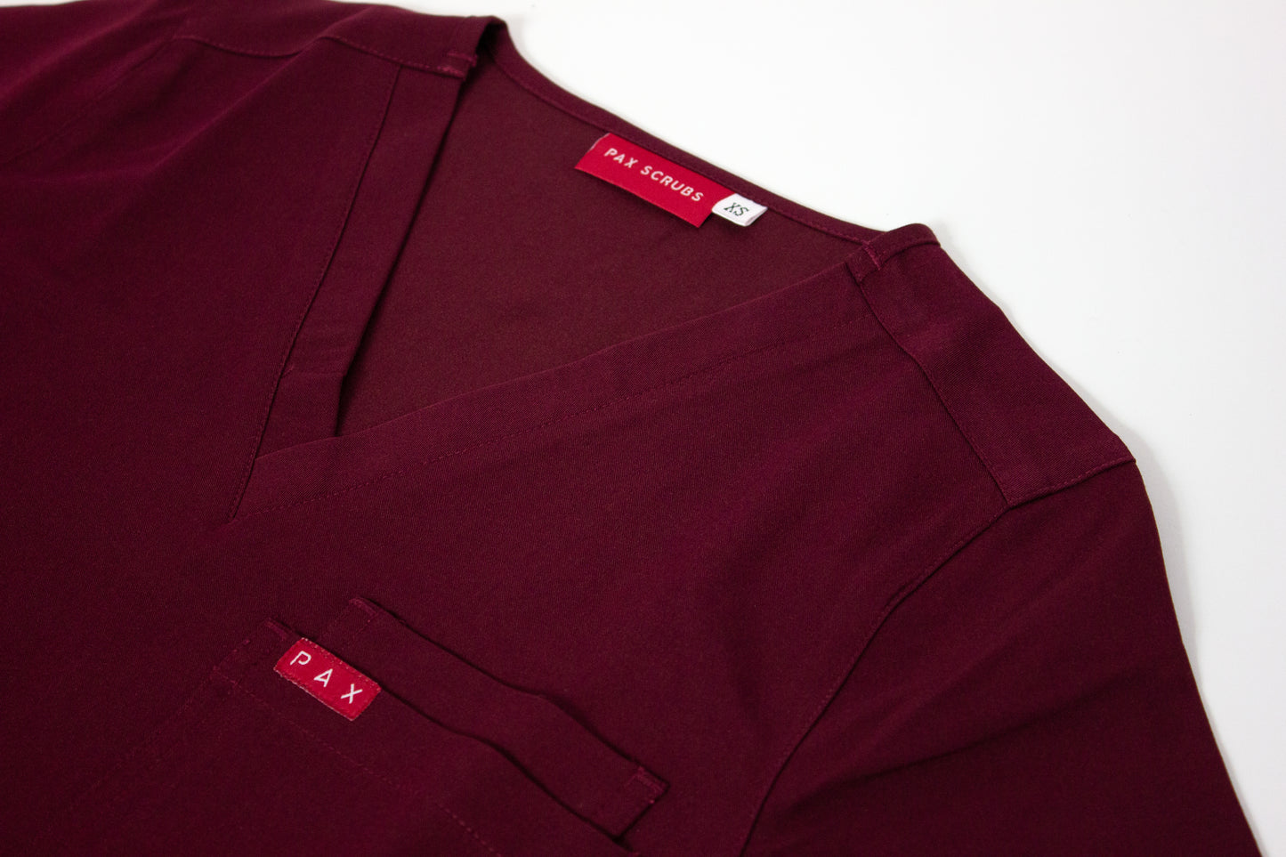 Close-up of a crimson V-neck PAX Primus scrub top with double breast pocket.