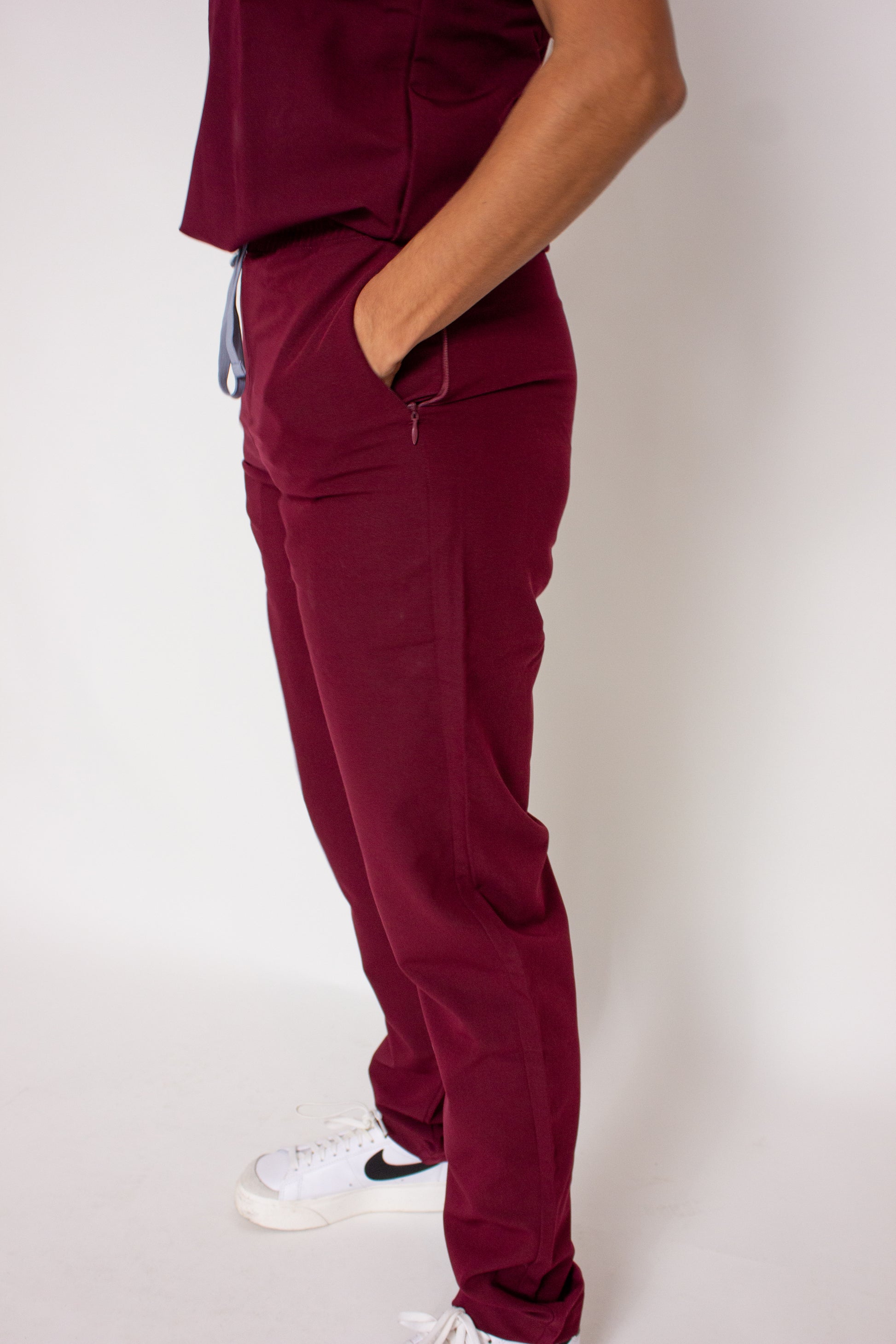 Side view of PAX Primus women's line crimson scrubs with hand in pocket and white sneakers.