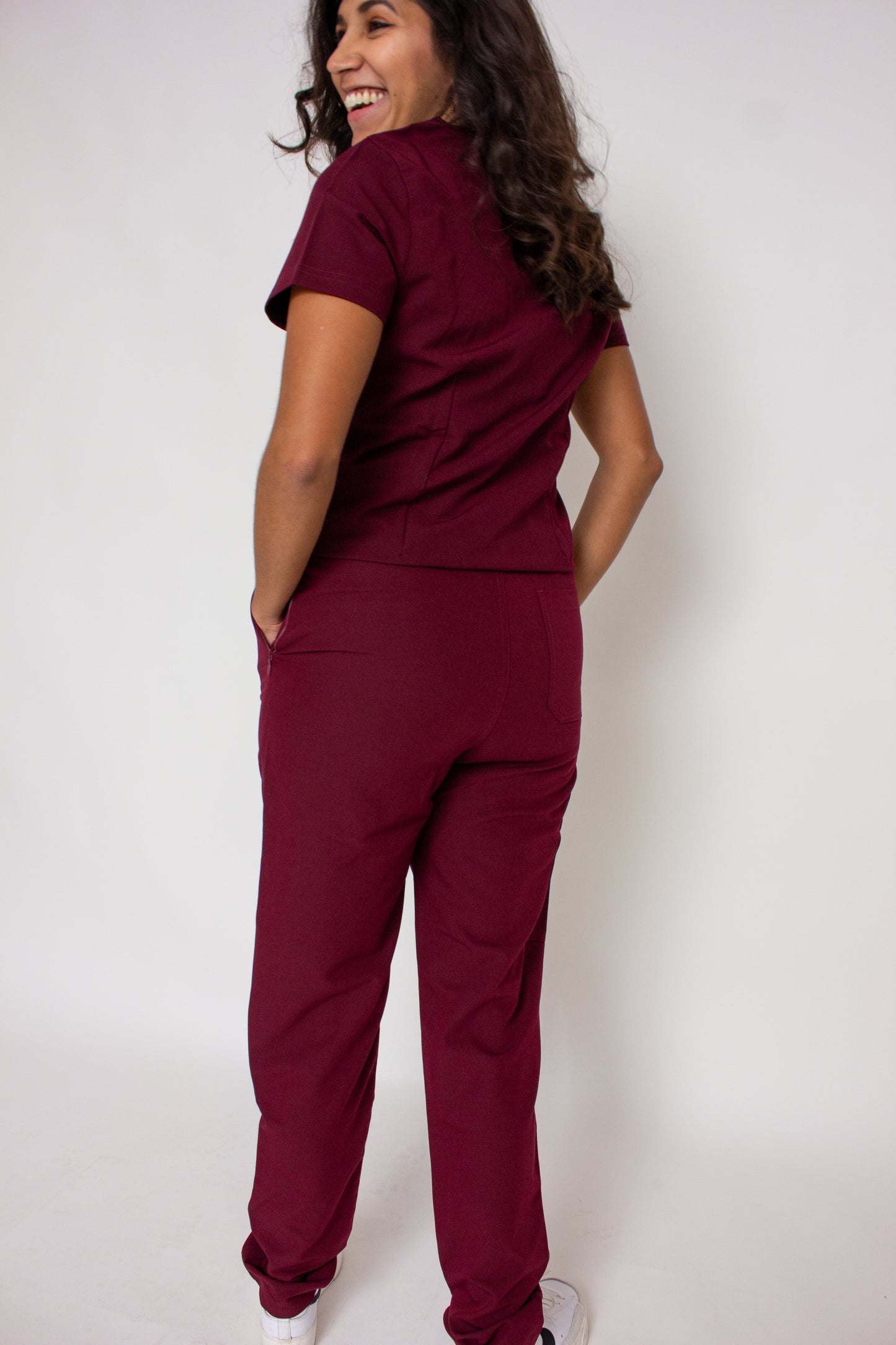 Smiling doctor in PAX Primus maroon scrubs with hands in pockets.