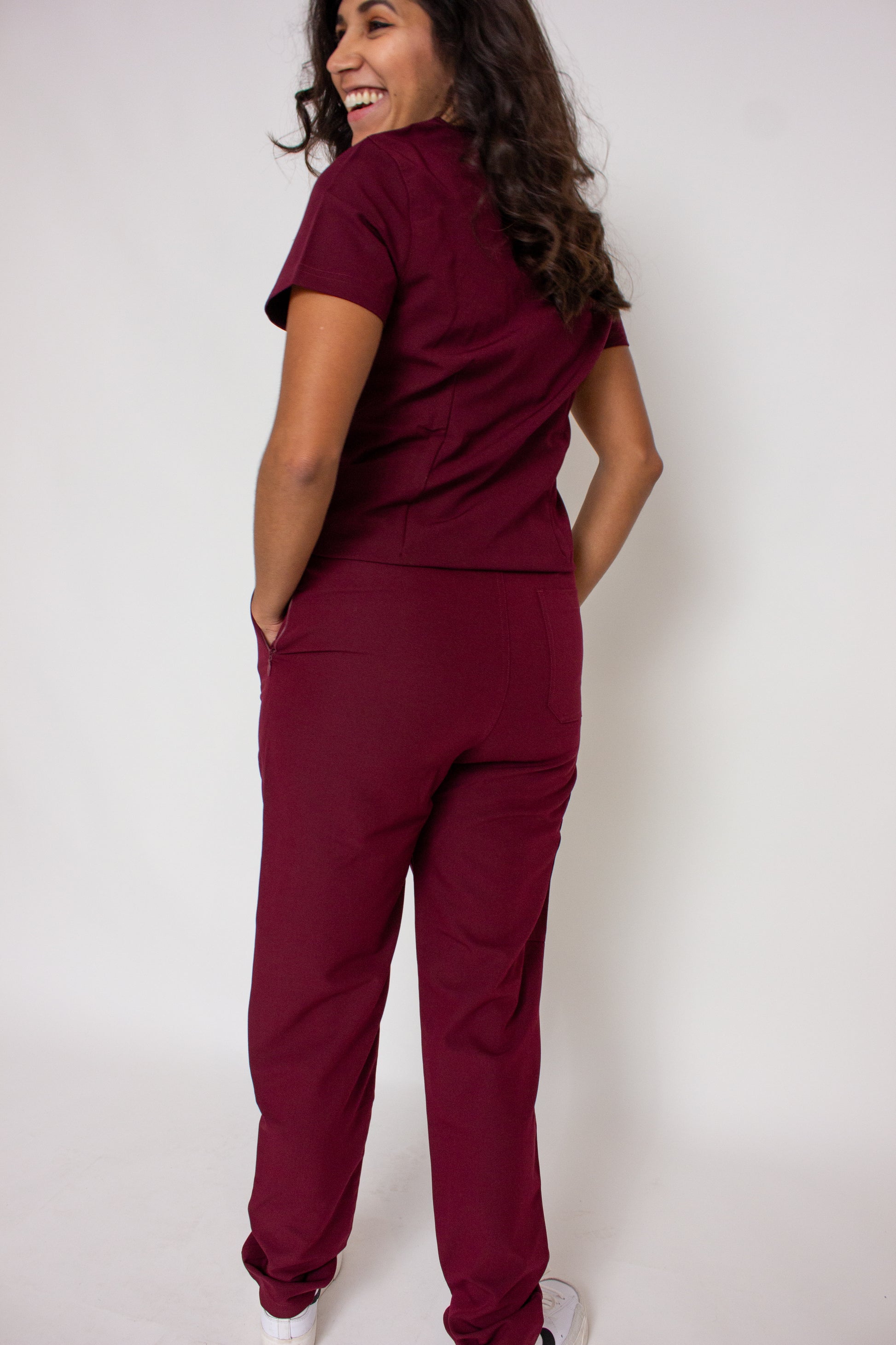 Smiling doctor in PAX Primus maroon scrubs with hands in pockets.