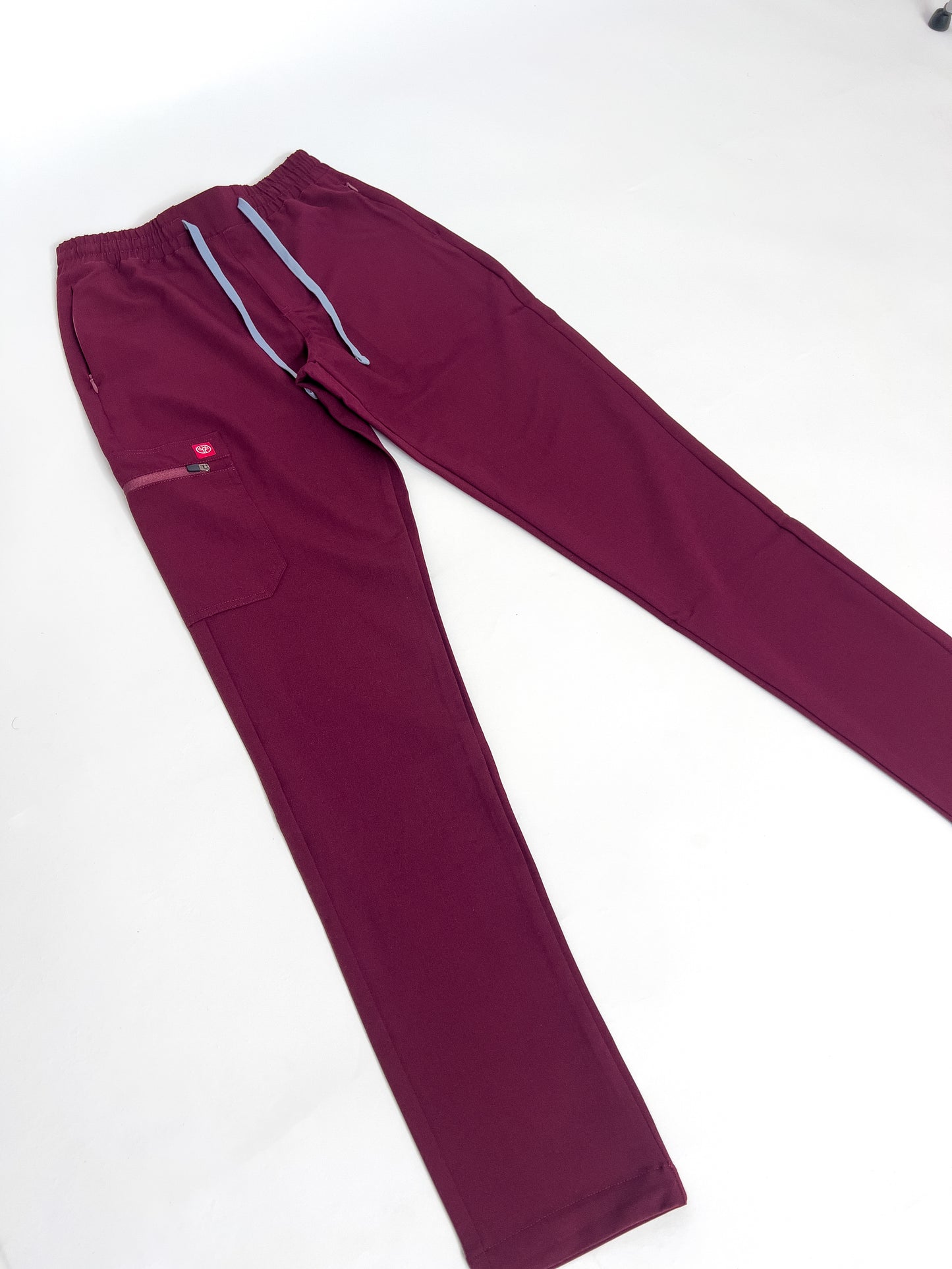 PAX Primus crimson scrub pants with grey drawstrings on white surface.