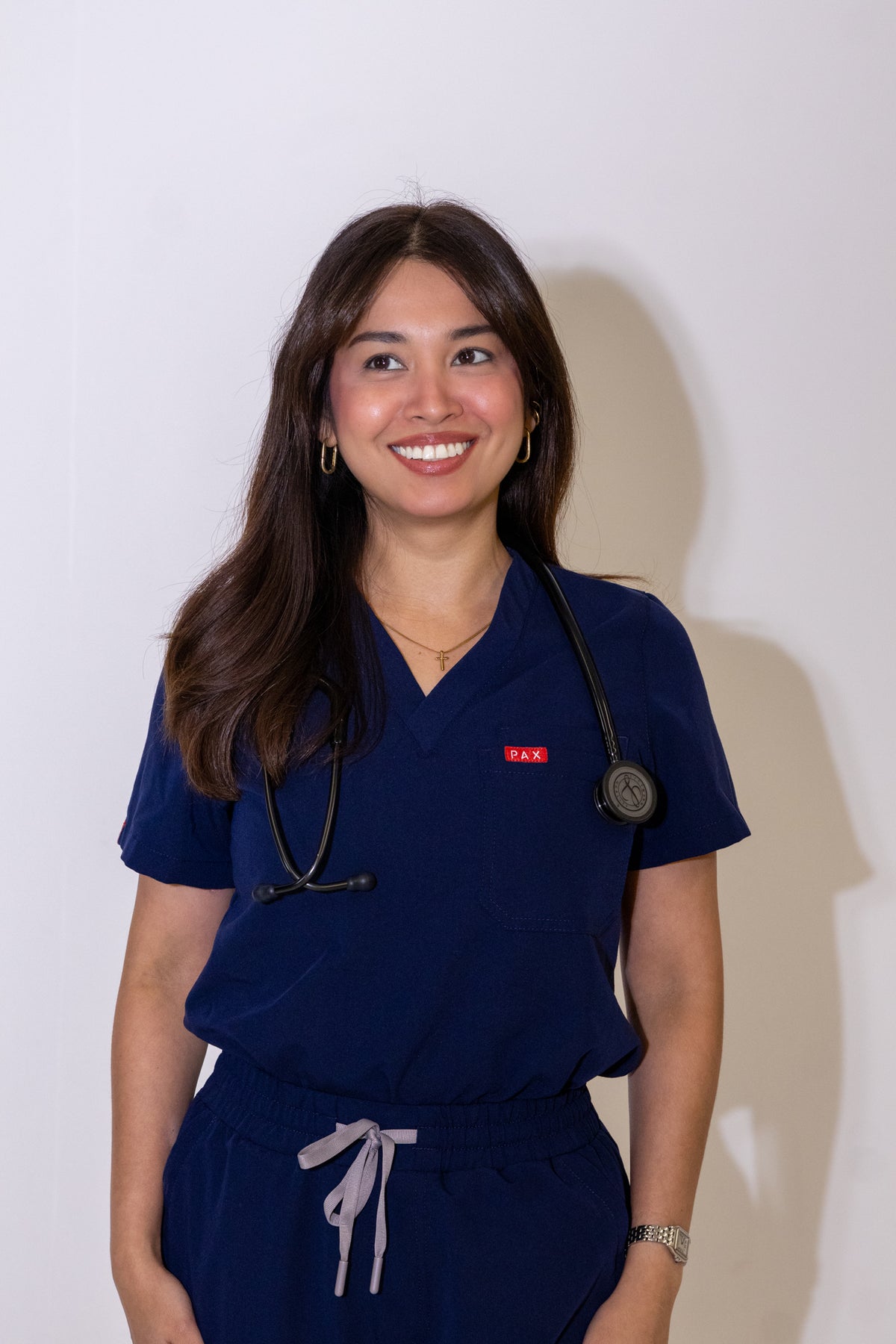 PAX Core Luma women's navy scrub top, front view on a model with a stethoscope