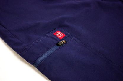 Close-up of the carmine red PAX tree logo on a blue scrub cargo pocket with zipper.