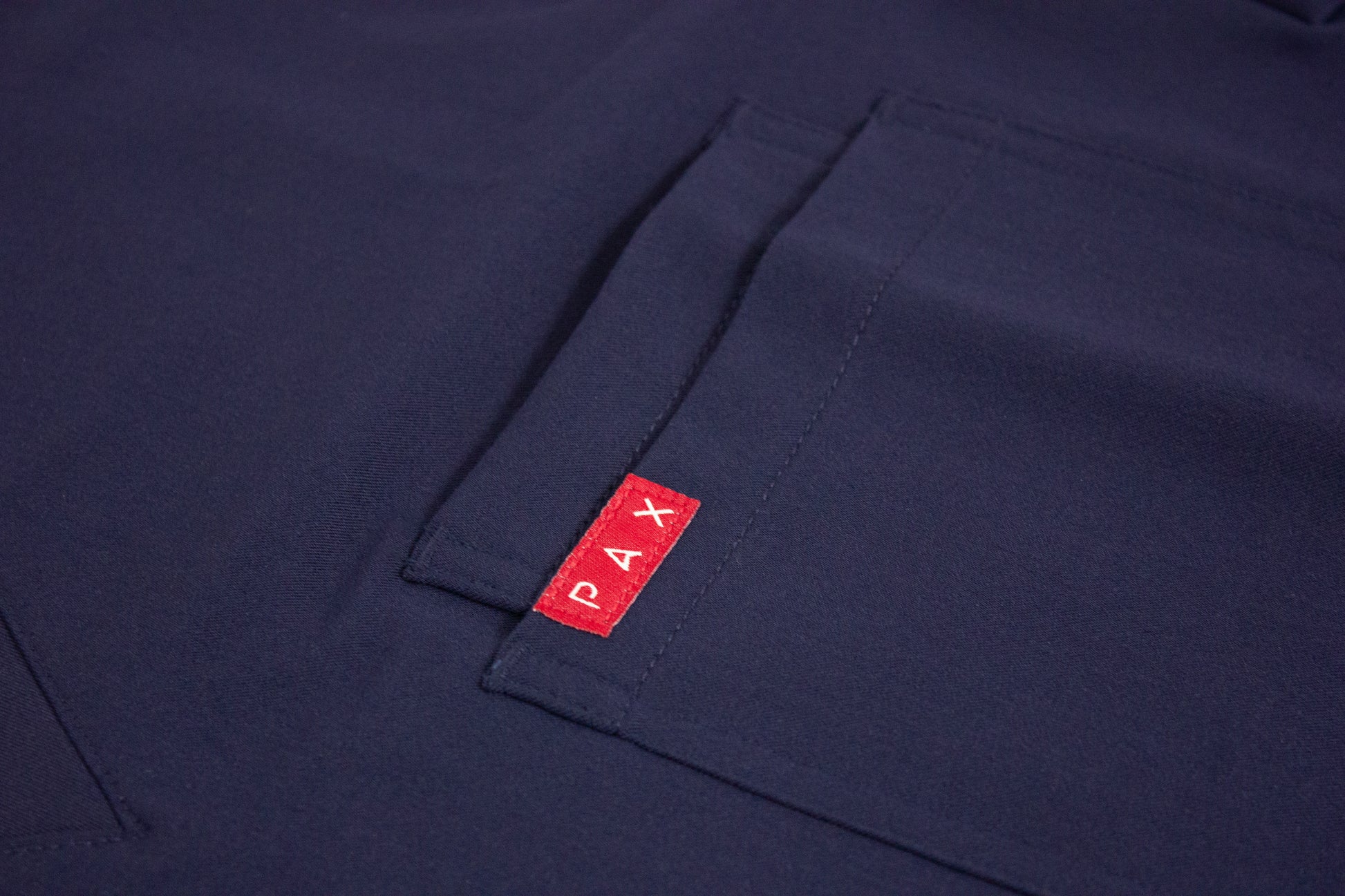 Detailed view of the PAX logo on the double breast pocket of a royal blue scrub top.
