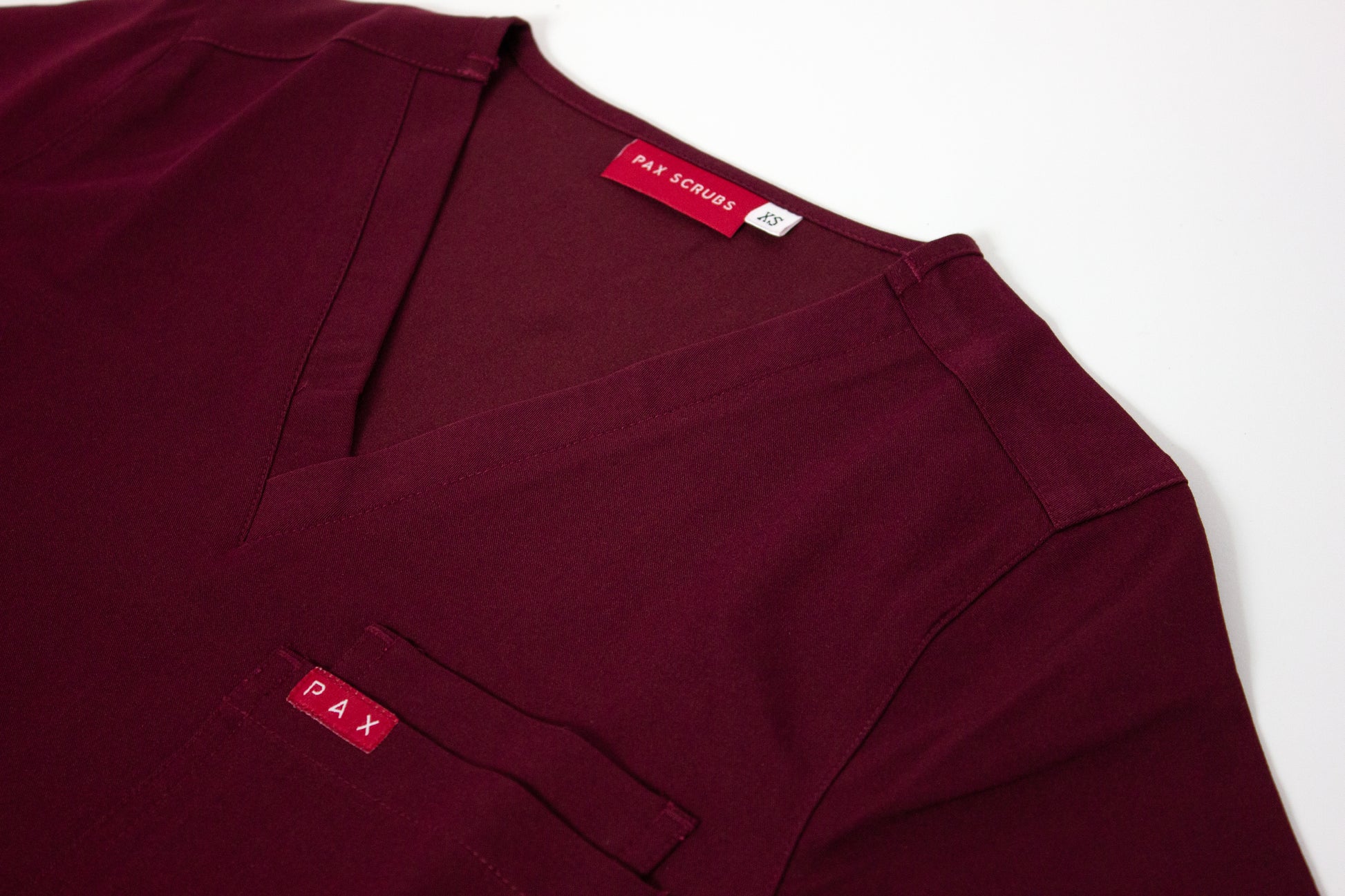 Close-up of a crimson V-neck PAX Primus scrub top with double breast pocket.