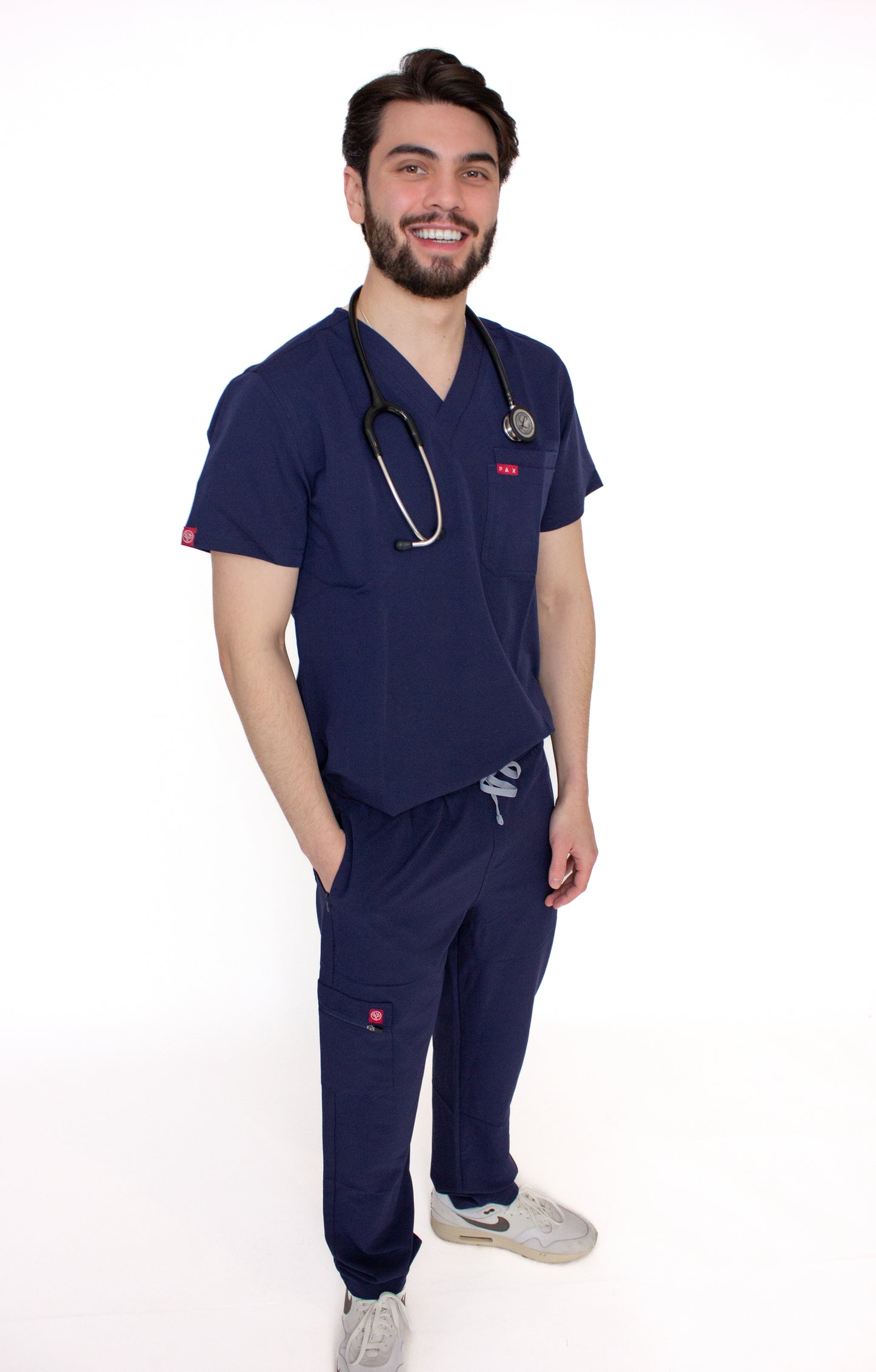 Smiling male healthcare worker in royal blue PAX scrubs with a stethoscope and sneakers.