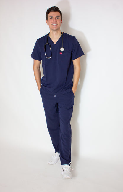 Smiling male doctor in a royal blue V-neck scrub top and matching bottoms.