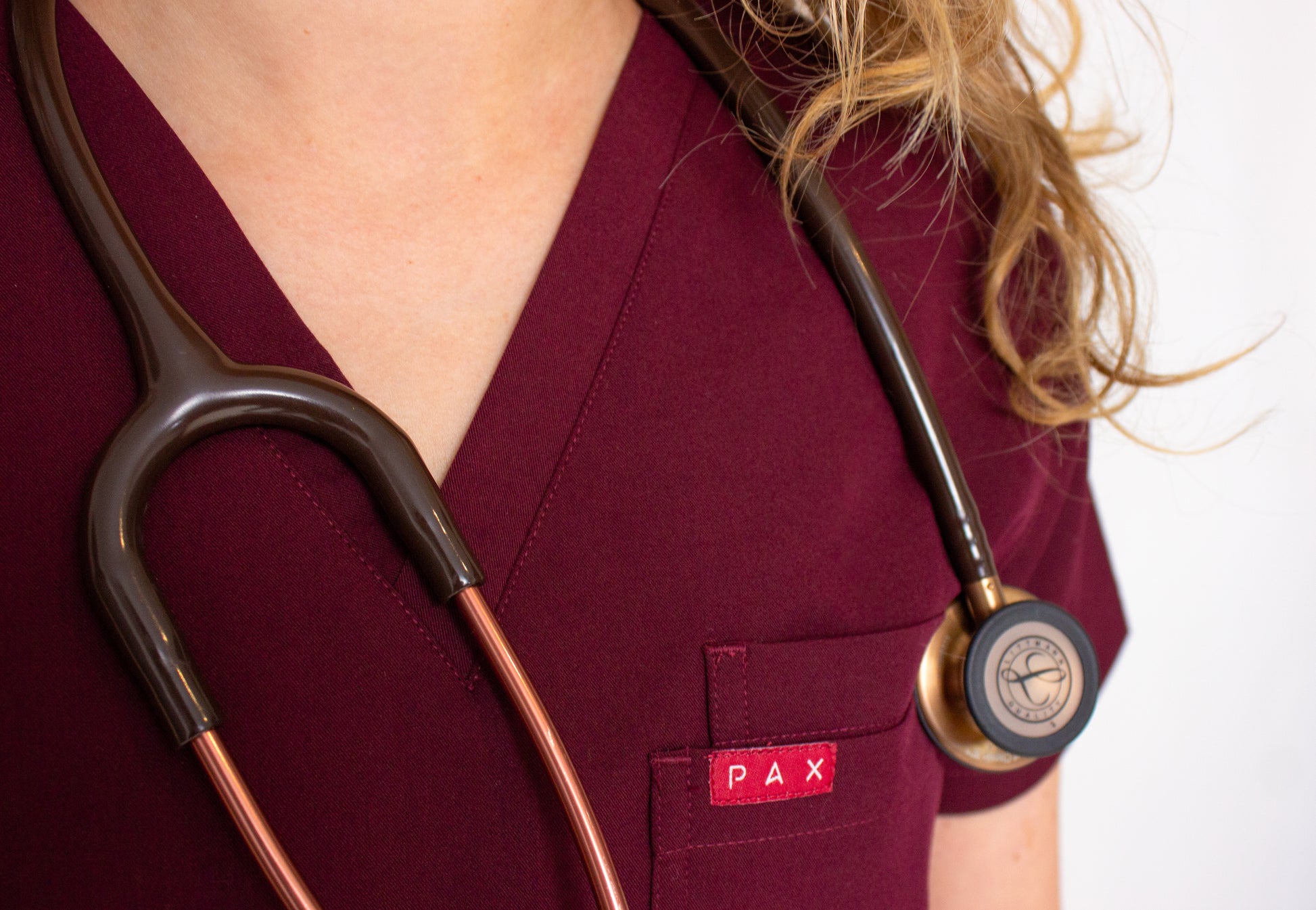 Close-up of carmine PAX logo on female crimson red scrub top's double breast pocket with stethoscope.