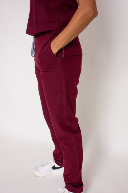 Side view of PAX Primus women's line crimson scrubs with hand in pocket and white sneakers. 