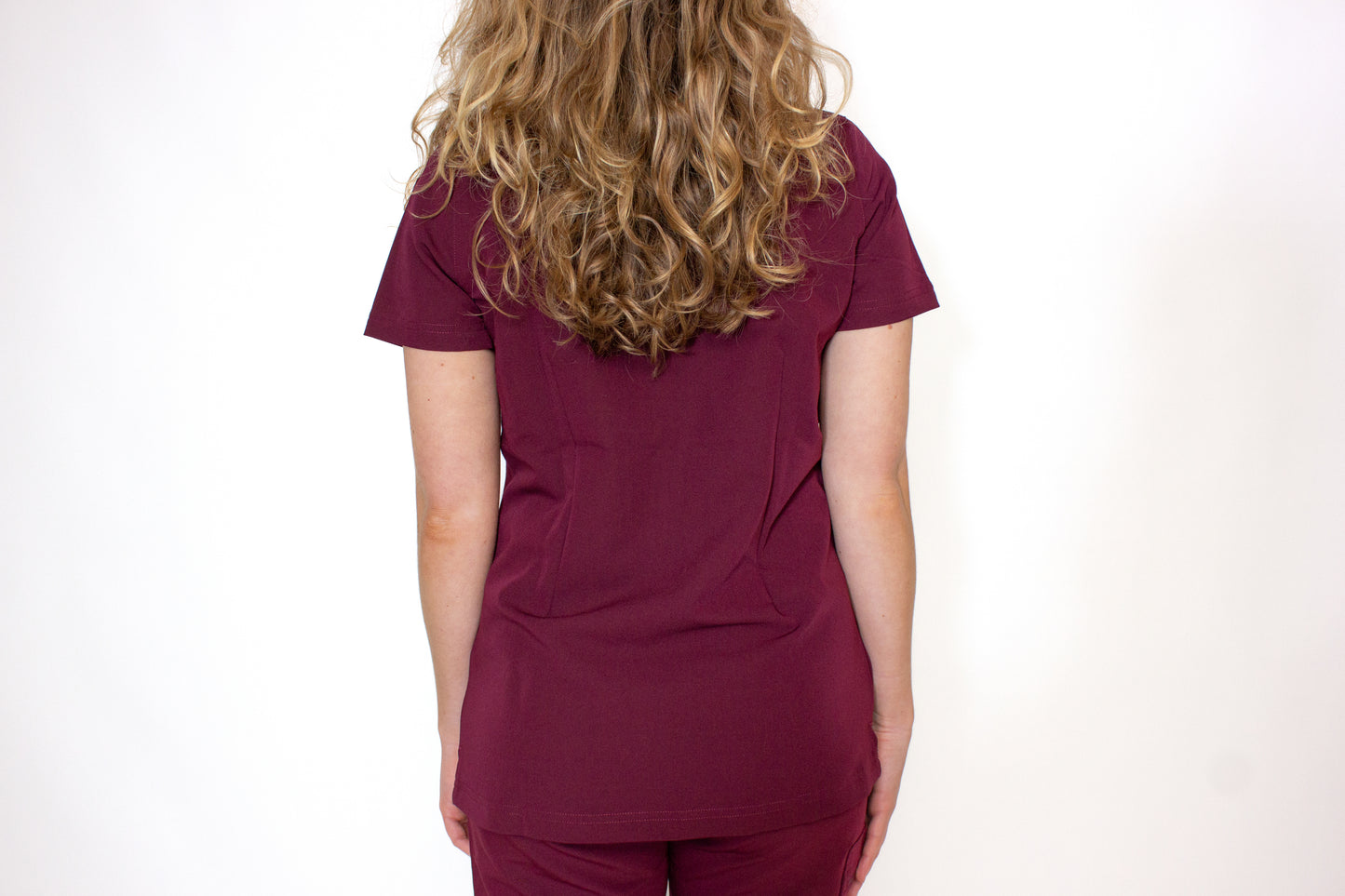Rear view of a crimson PAX scrub top on a female with curly hair.