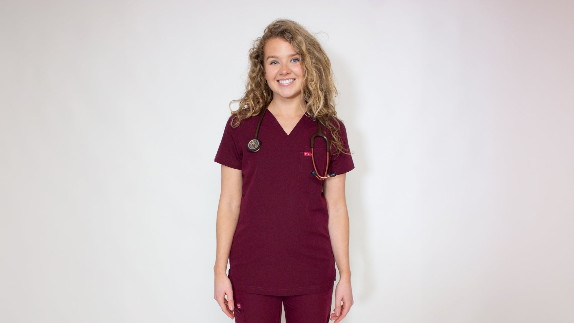 Female medical professional in a fitted crimson PAX Primus scrubs top with matching bottoms.