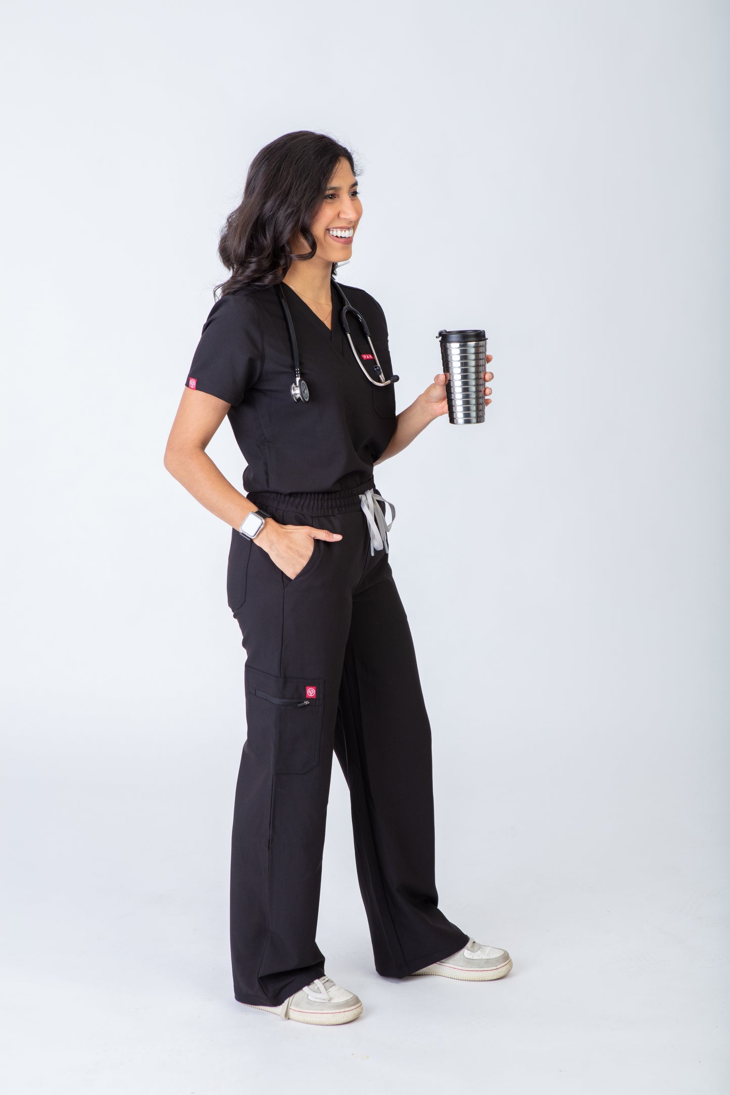 Person wearing black medical scrubs holding a coffee cup on a white background