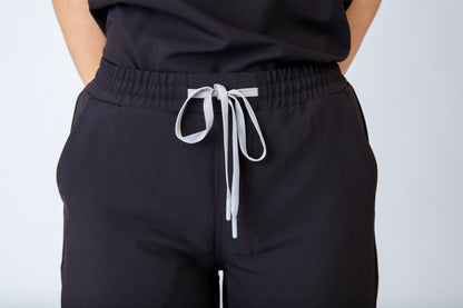 Black scrubs pants with a white drawstring on a plain background
