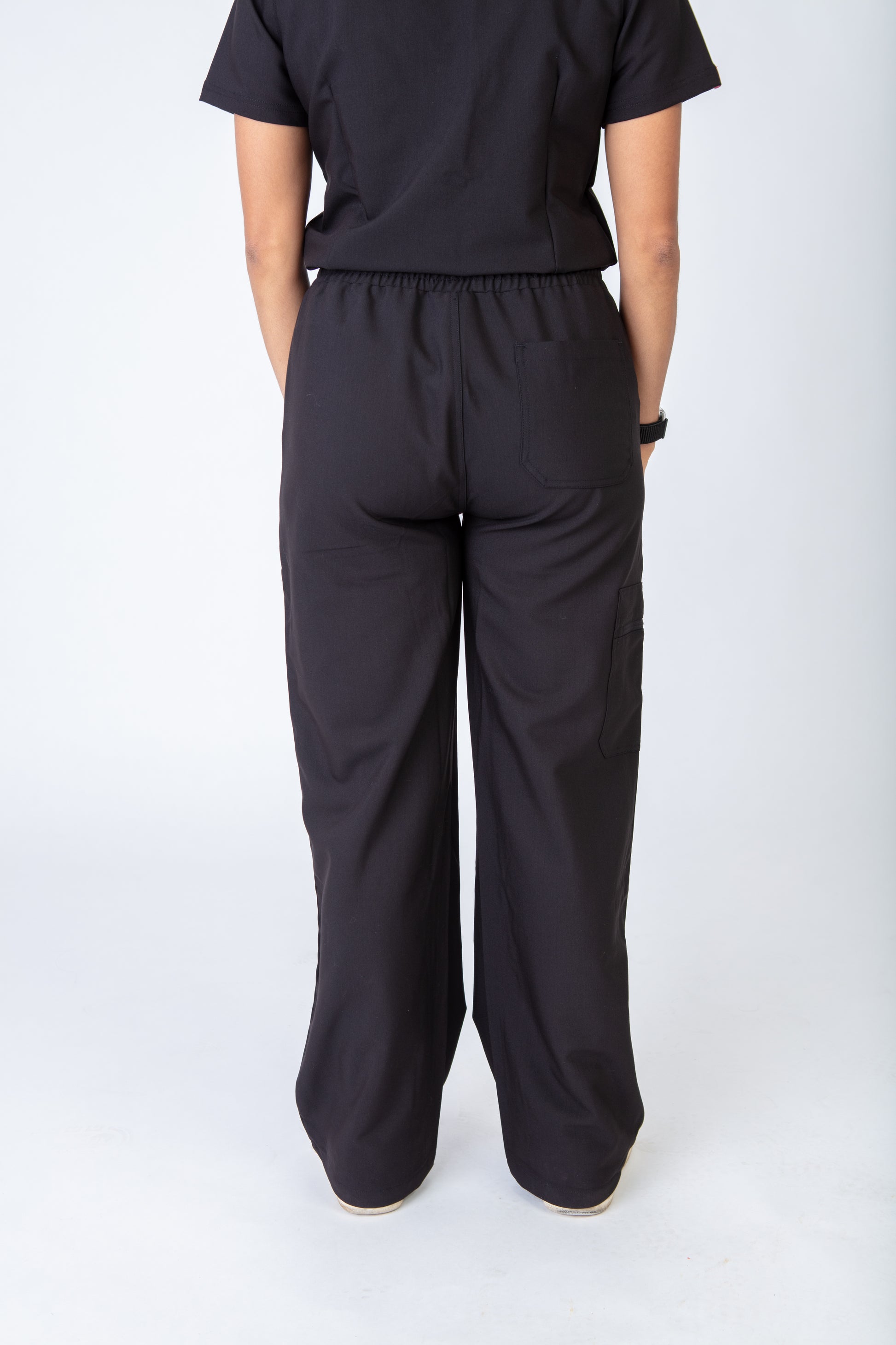 Person wearing black scrubs pants and a black scrubs top on a white background