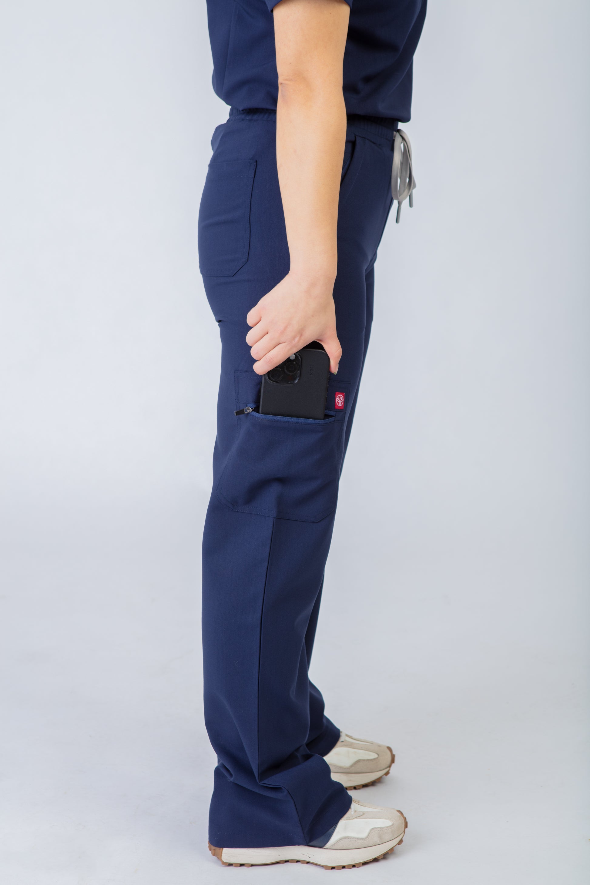 Person wearing navy blue scrubs pants with a pocket on a light gray background