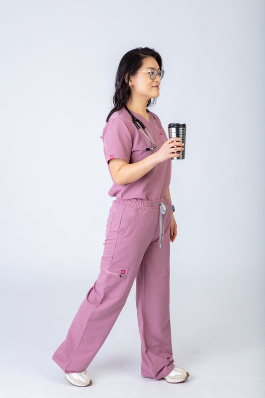 Person wearing pink medical scrubs holding a coffee cup on a white background