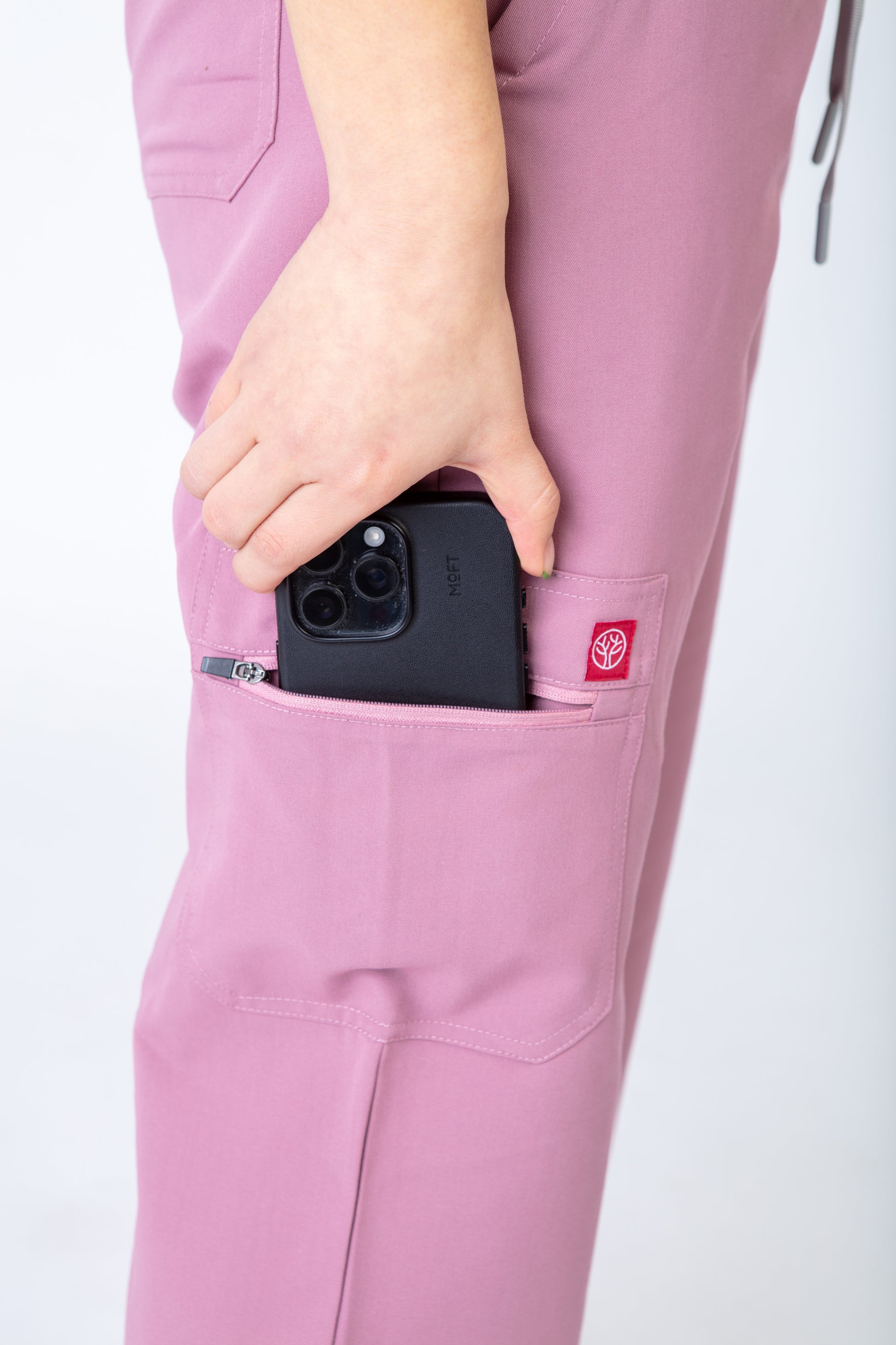 Person wearing pink scrubs with a phone in a pocket on a white background