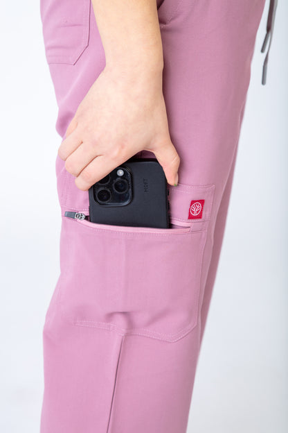 Person wearing pink scrubs with a phone in a pocket on a white background
