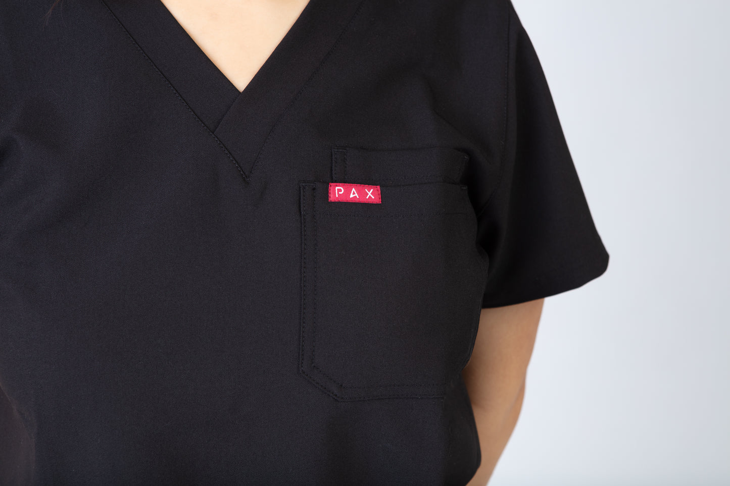 Black scrub top with a red 'PAX' logo on the chest pocket against a white background