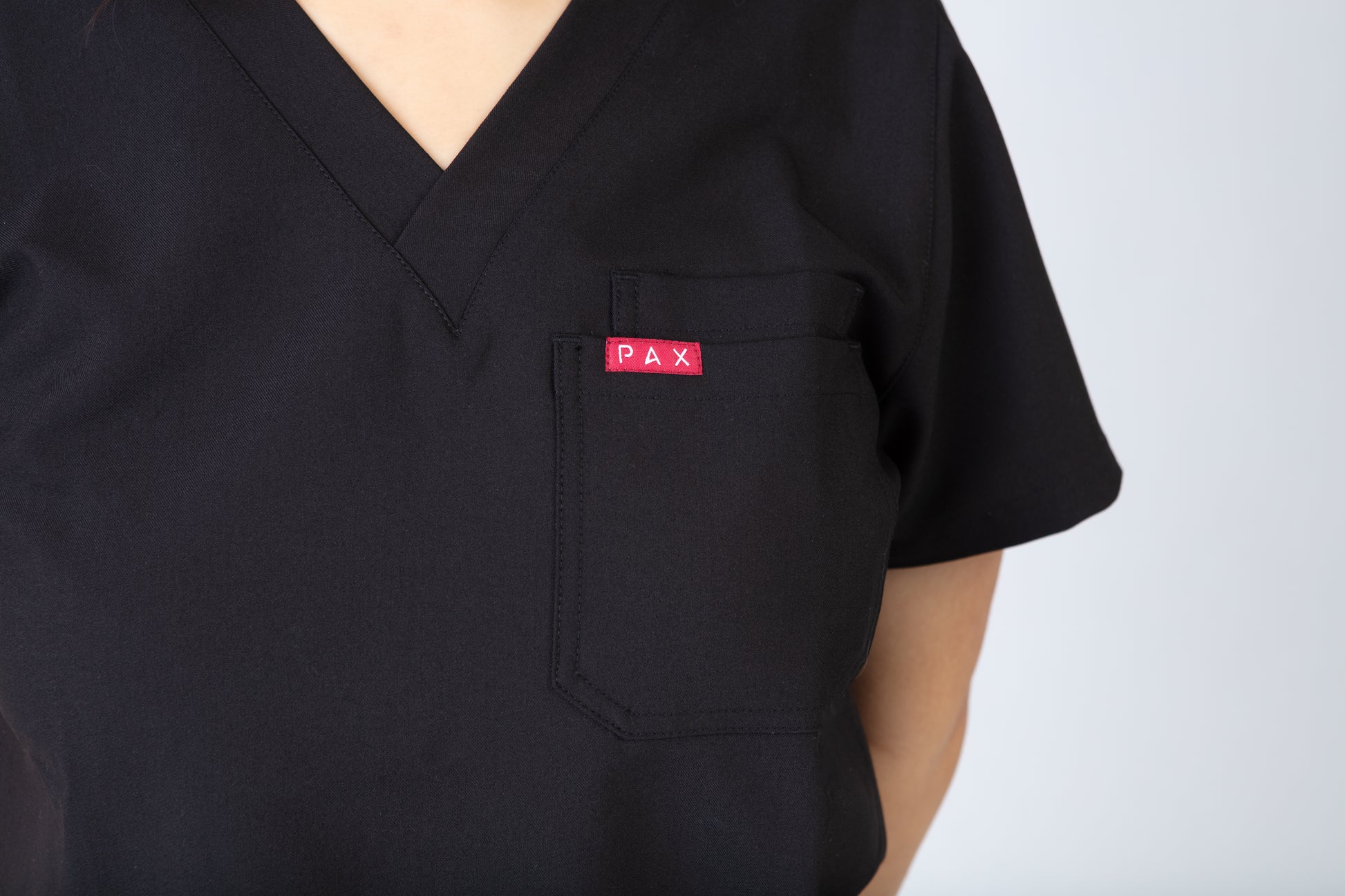 Black scrub top with a red 'PAX' logo on the chest pocket against a white background