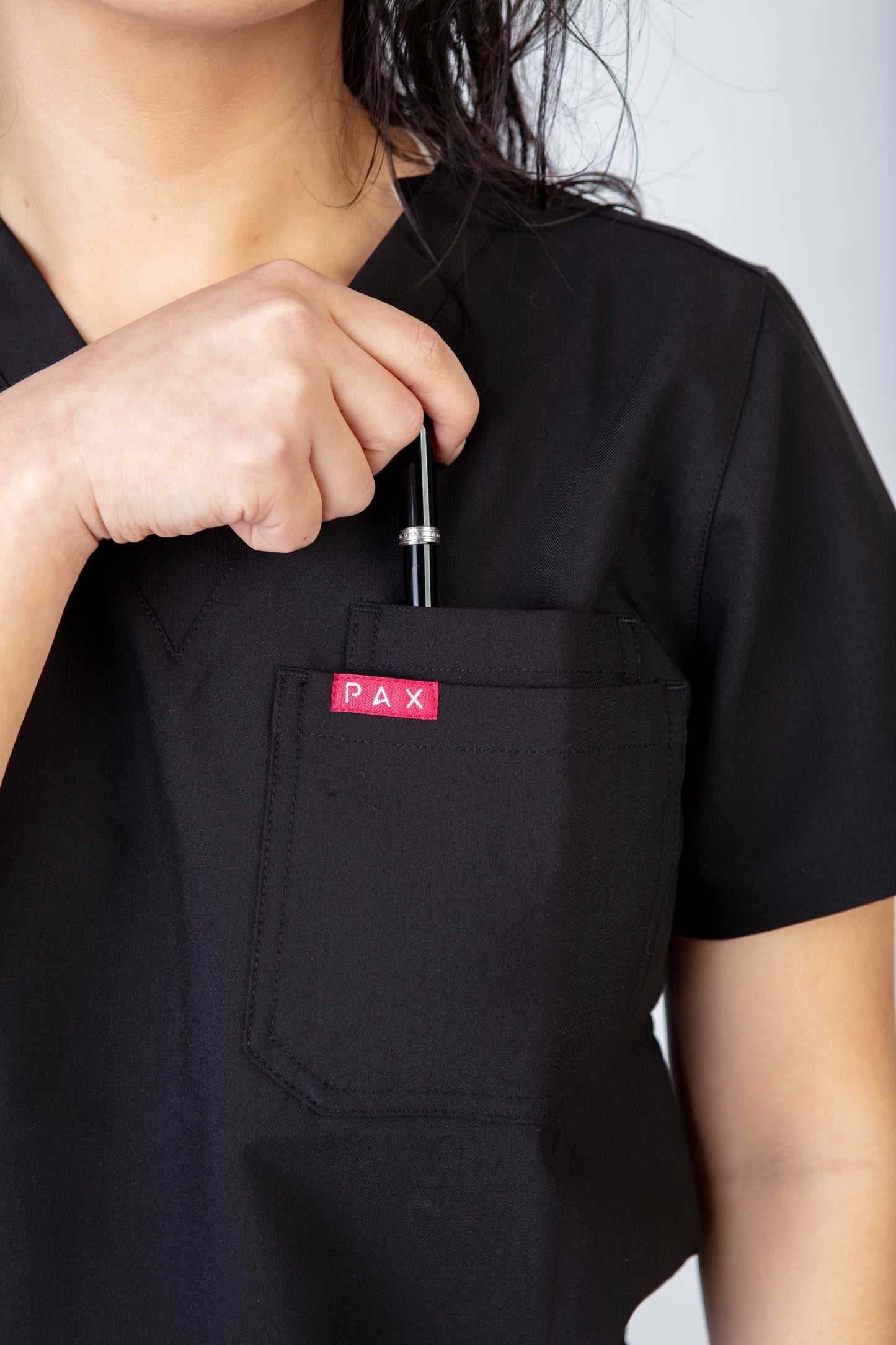 Person wearing a black scrub top with a red 'PAX' logo on the chest pocket.