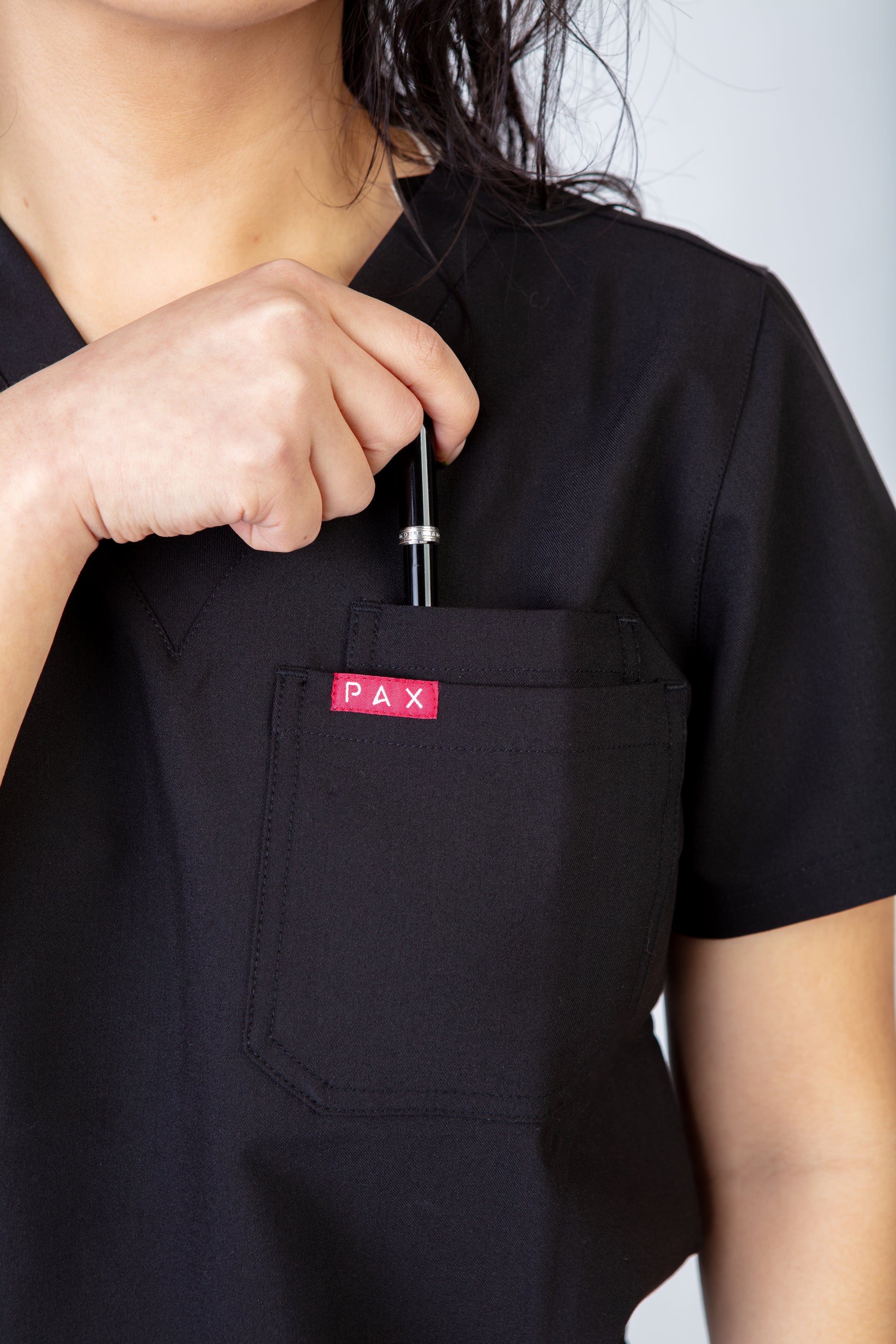 Person wearing a black scrub top with a red 'PAX' logo on the chest pocket.
