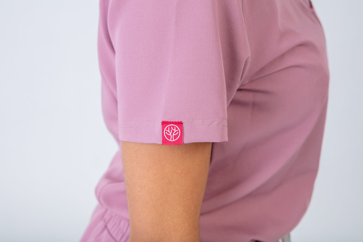 Pink scrub top with a logo on the chest pocket against a white background